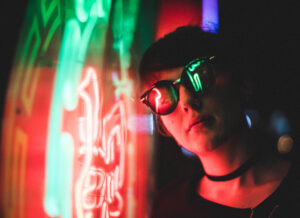 Image: Person wearing sunglasses standing by the colorful neon light